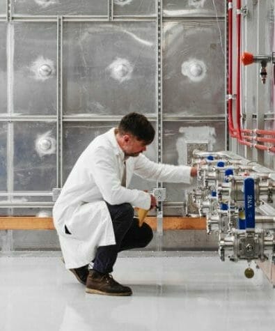 man in lab coat kneels in front of technical equipment